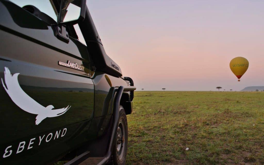 A hot air balloon over the Masai Mara seen from an andBeyond game drive vehicle