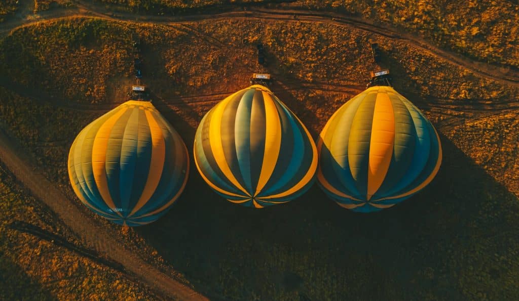 Looking down from a balloon onto four striped hot air balloons floating above the flat Serengeti plains